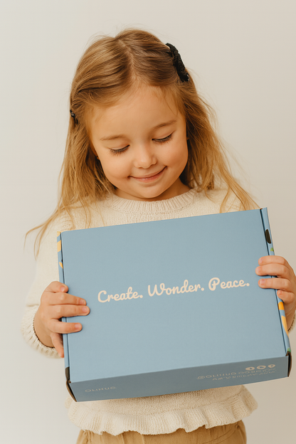 Smiling child holding OLiHUG blue subscription box with joy. Montessori-inspired creative kit for kids that promotes mindfulness, focus, and screen-free fun. Beautiful family-friendly gift for birthdays or holidays, encouraging creativity and emotional connection through hands-on play.