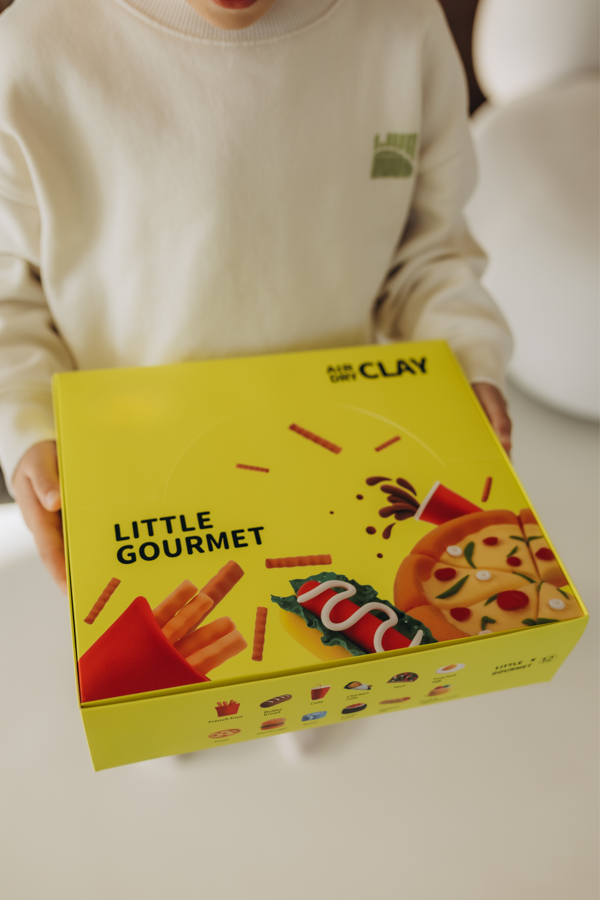 Happy child holding the Little Gourmet Air Dry Clay Kit gift box. A joyful Montessori-inspired activity box designed to spark imagination, confidence, and creativity. Perfect for birthdays, gifts, and screen-free family time. Eco-friendly, non-toxic materials for worry-free creative play.